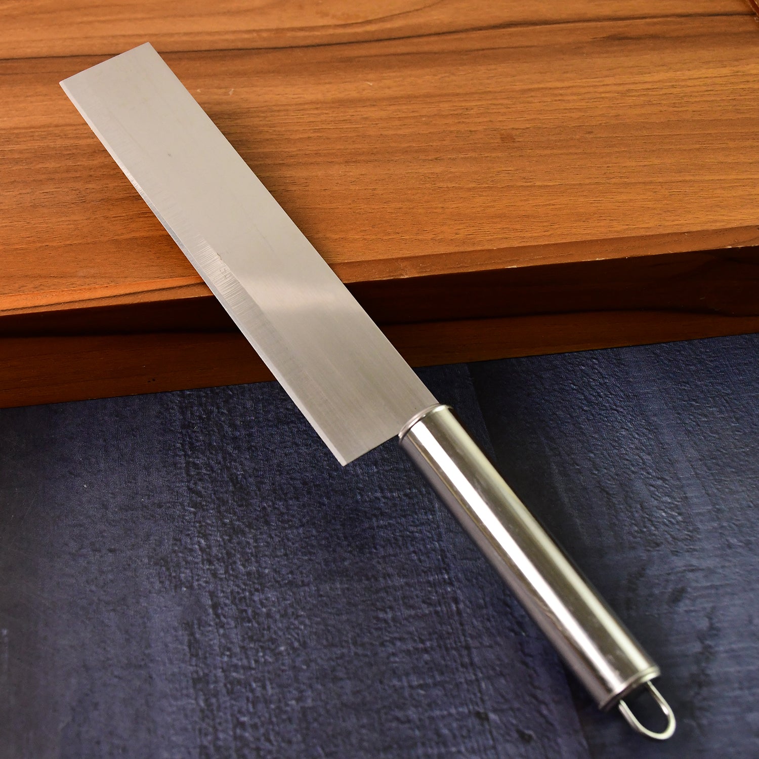 The Wukusy Professional-grade Stainless Steel Vegetable Cleaver Knife 1 Pc, featuring a rectangular blade and metal handle, rests on a dark countertop beside a wooden cutting board.